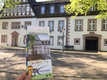 Flyer für den Beverunger Stadtspaziergang vor einem Fachwerkgebäude auf gepflastertem Platz.
