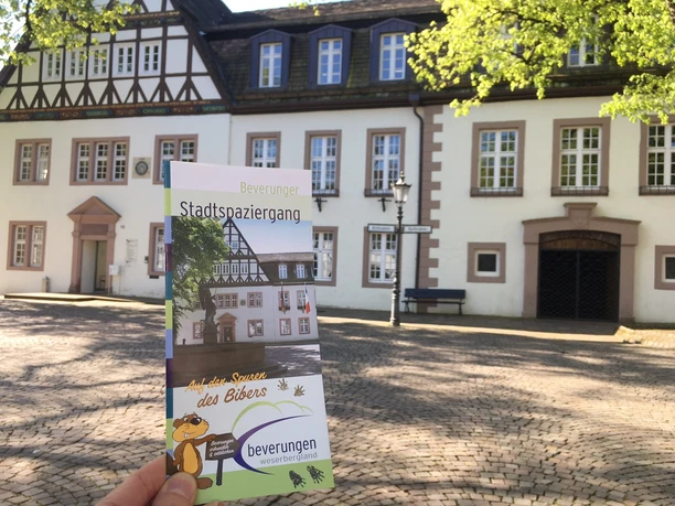 Beverunger Stadtspaziergang Flyer für den Beverunger Stadtspaziergang wird vor einem Fachwerkgebäude auf gepflastertem Platz präsentiert..