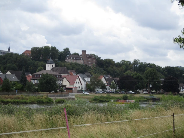 Blick auf Herstelle Blick auf Herstelle mit der historischen Burg und dem Dorf am Weserufer, umgeben von grüner Landschaft.