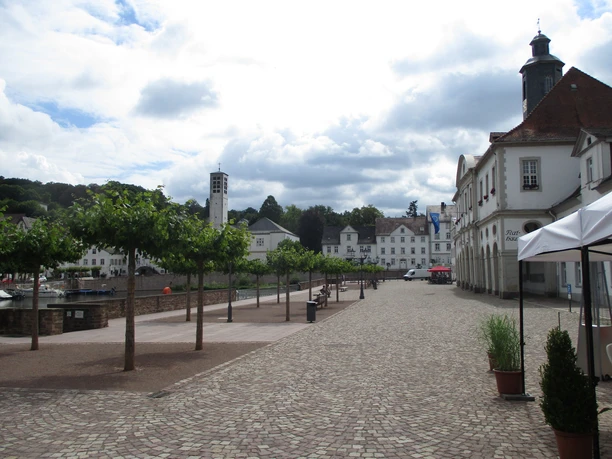 Hafen in Bad Karlshafen Kopfsteinpflasterplatz in Bad Karlshafen, flankiert von Bäumen, historischen Gebäuden und Hafenansicht.