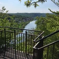 Aussichtsplattform mit Blick auf den Fluss Weser, umgeben von grünen Hügeln und üppigem Laub.