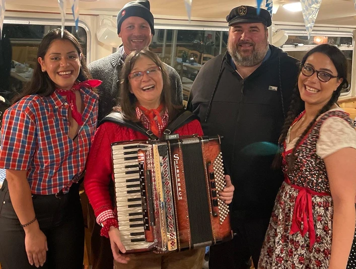 Wally.jpg Eine fröhliche Gruppe von Menschen in traditioneller bayerischer Kleidung mit einer Akkordeonspielerin.