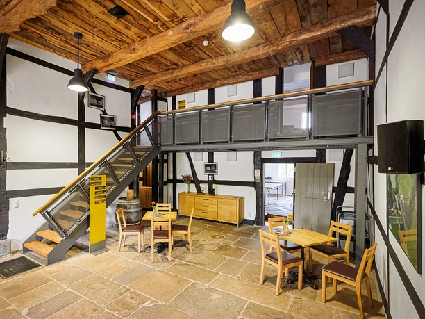 Emscherquellhof, Holzwickede Ein rustikaler Innenraum eines Fachwerkhauses mit Holzbalken, Treppe, Holzmöbeln und Steinboden.
