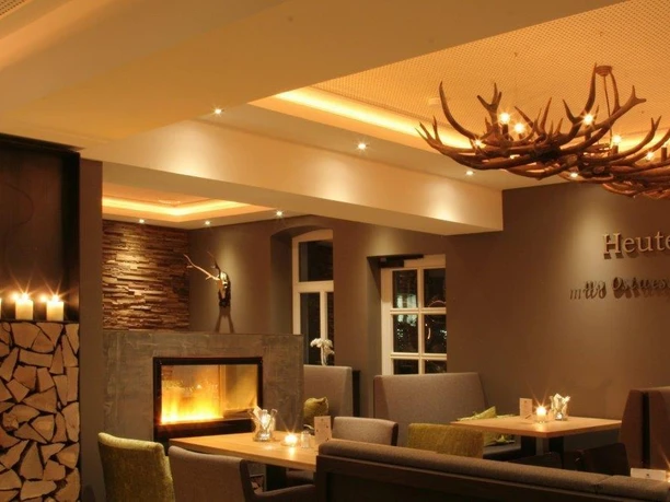 Gemütliche Restaurant-Innenansicht mit Kamin, modernen Sitzgruppen und dekorativer Hirschgeweih-Lampe.