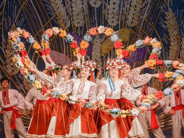 Ukrainische Tänzerinnen und Tänzer in traditioneller Kleidung bilden Herzformen mit Blumenkränzen.