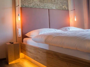 Gemütliches Hotelzimmer mit einem modernen Doppelbett, warmem Licht und stilvoller Holzverkleidung.