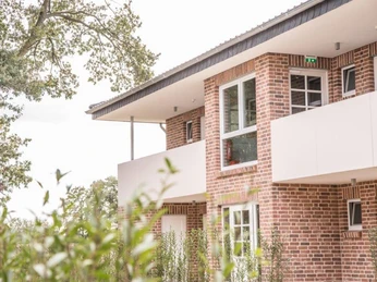 Backstein-Fassade eines modernen, zweistöckigen Gebäudes mit großen Fenstern und umliegendem Grün.