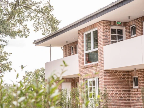 Innenhof Hotel Backstein-Fassade eines modernen, zweistöckigen Gebäudes mit großen Fenstern und umliegendem Grün.