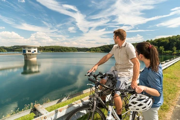 Radfahren an der Dhünntalsperre Radfahrer genießen den Blick auf einen malerischen Stausee unter blauem Himmel in Wermelskirchen.