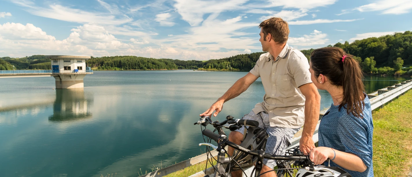 Radfahren an der Dhünntalsperre Radfahrer genießen den Blick auf einen malerischen Stausee unter blauem Himmel in Wermelskirchen.