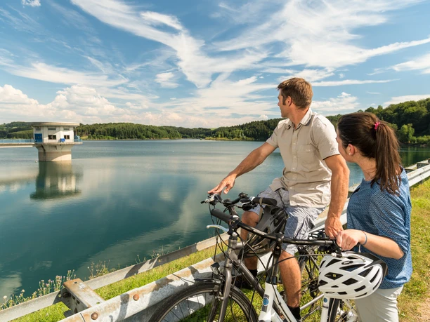 Radfahren an der Dhünntalsperre Radfahrer genießen den Blick auf einen malerischen Stausee unter blauem Himmel in Wermelskirchen.
