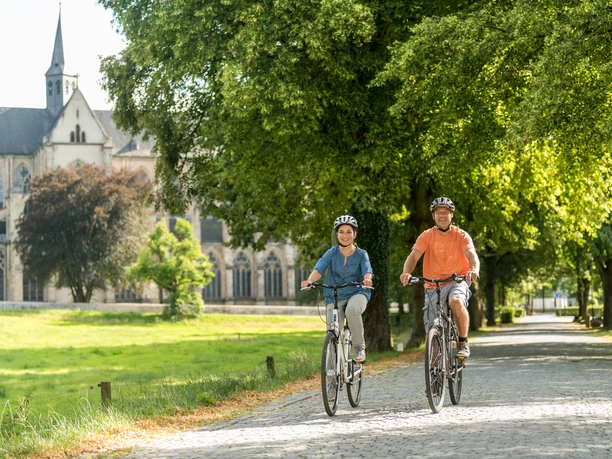 Rad fahren in Altenberg Zwei Radfahrer fahren auf einem sonnigen Weg vor einer alten Kirche in einer grünen Landschaft.