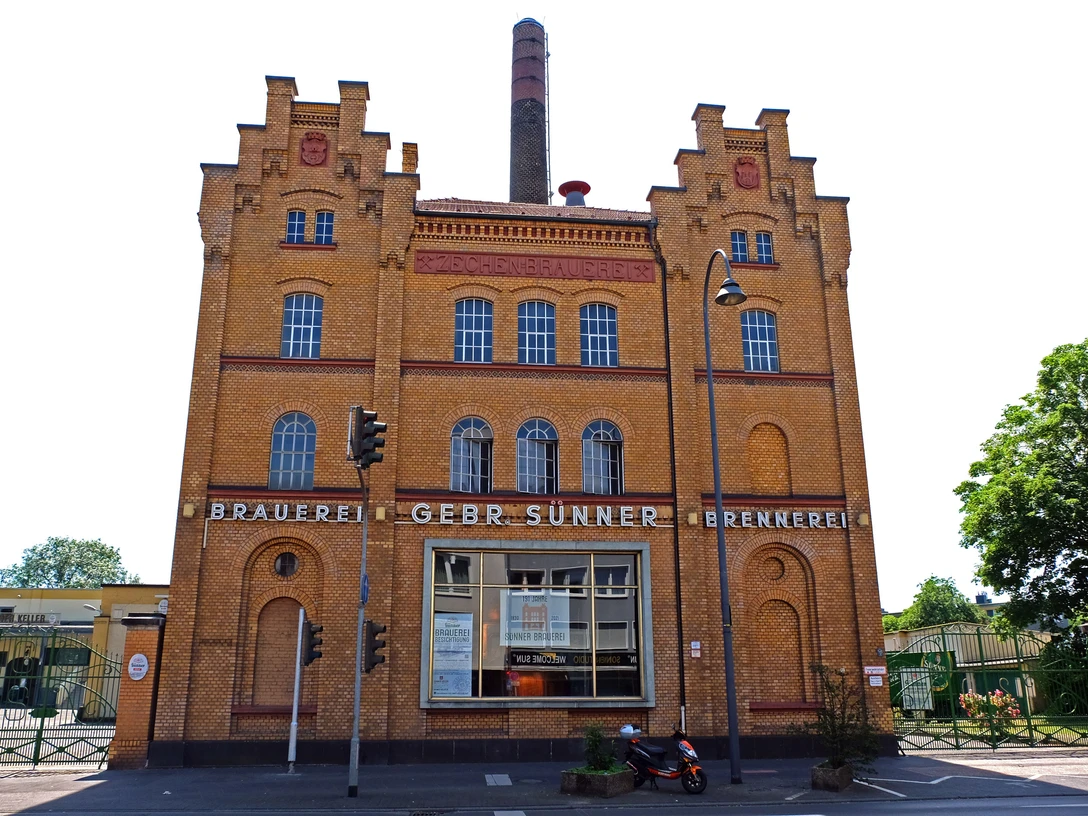 Brauwelt in Köln-Kalk Historisches Brauereigebäude in Köln-Kalk mit markanter Ziegelfassade und großen Fenstern bei blauem Himmel.Historic brewery building in Cologne-Kalk with striking brick façade and large windows under a blue sky.