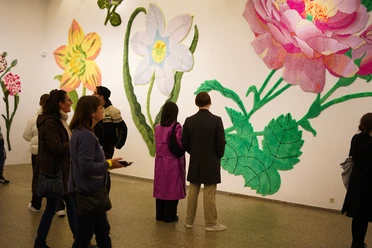 Visitors observe oversized colourful flower artworks on a gallery wall.