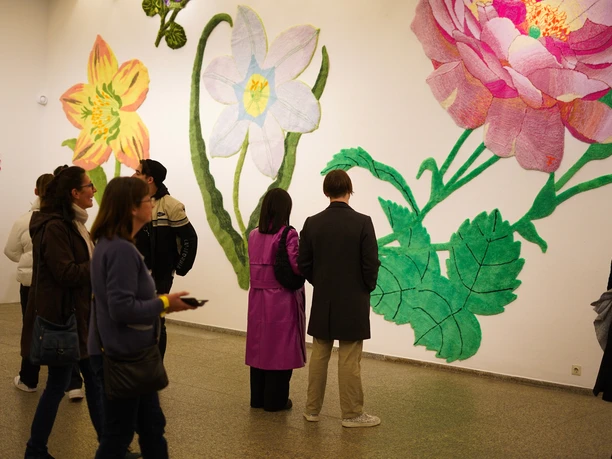 Visitors observe oversized colourful flower artworks on a gallery wall.
