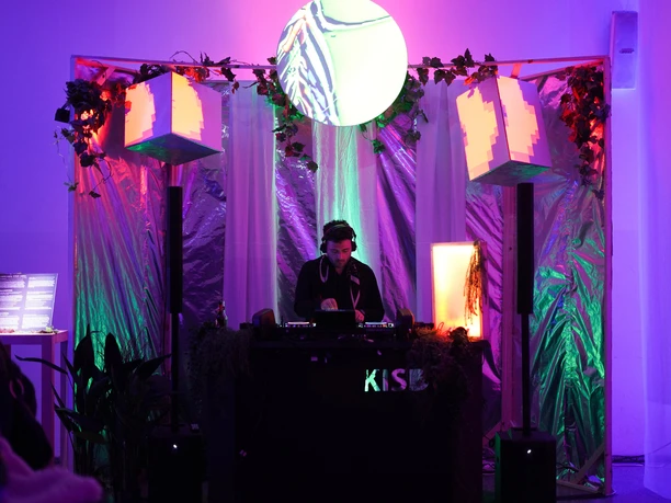DJ performing under colourful lights with plants and geometric decor in a museum setting