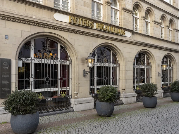 Peters Brauhaus Historic façade of Peters Brauhaus in Cologne, adorned with round windows, sandstone façade and iron decorations. Planters line the paved walkway.