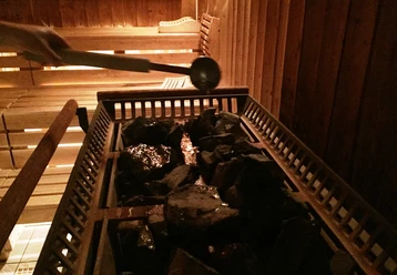 In einer Sauna wird Wasser mit einer Kelle auf erhitzte Steine gegossen, um Dampf zu erzeugen.