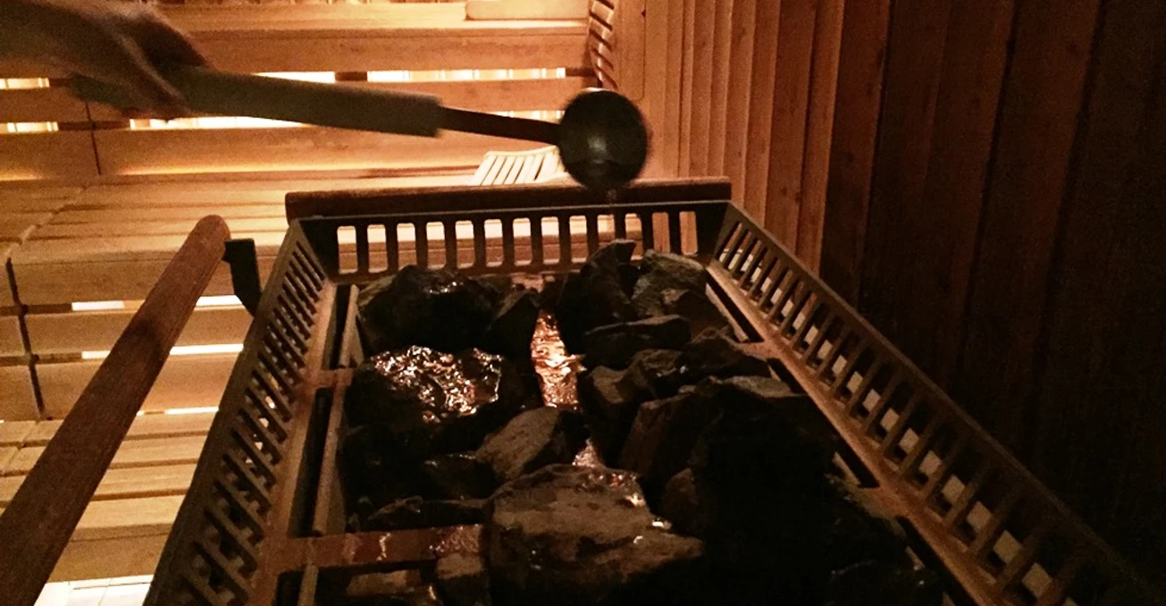 In einer Sauna wird Wasser mit einer Kelle auf erhitzte Steine gegossen, um Dampf zu erzeugen.