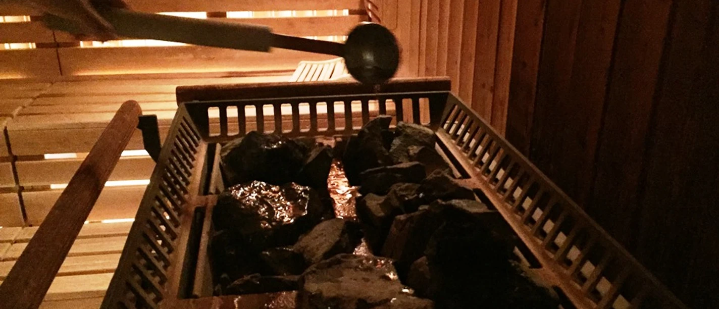 In einer Sauna wird Wasser mit einer Kelle auf erhitzte Steine gegossen, um Dampf zu erzeugen.