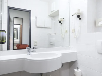 Badezimmer im ACHAT Hotel Monheim am Rhein Helles, modernes Badezimmer mit großem Spiegel, Waschbecken, Haartrockner und Handtuchhalter.