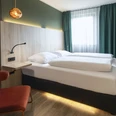 Business Doppelzimmer im ACHAT Hotel Monheim am Rhein Doppelzimmer mit modernem Design, geräumigem Bett, schickem Sessel, Holzdetails und eleganter Beleuchtung.