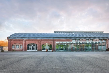 Rohrmeisterei, Schwerte Altes Backsteingebäude mit Glas-Anbau und großem gepflasterten Vorplatz bei bedecktem Himmel.