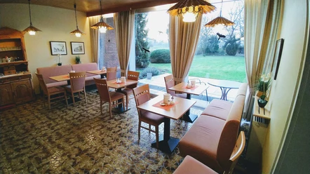Hotel-Pension Bevertal Garni - Frühstücksraum Frühstücksraum mit Tischgruppen, gepolsterten Stühlen und Sitzbänken, Blick in den grünen Garten, an der Wand ein Holzbuffet und Bilder