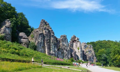 Externsteine_CC_BY_SA_BadSalzuflen_KerstinPaar.jpg Sandsteinfelsen in Norddeutschland, bekannt als Externsteine, umgeben von Wald und Grünflächen.