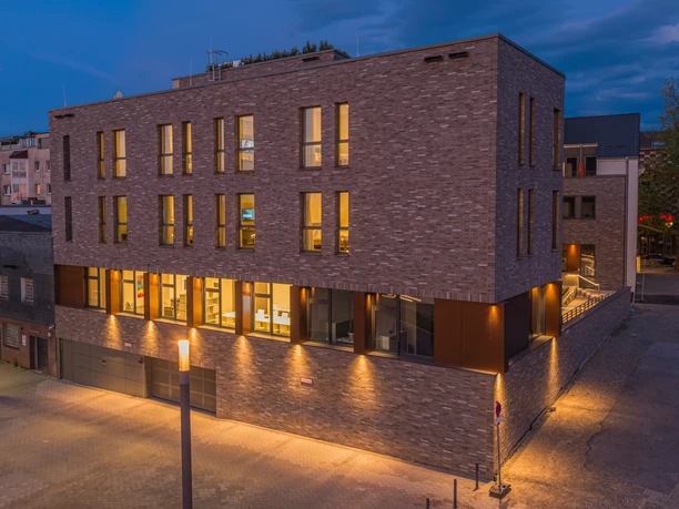 Hotel Neues Pastorat in Heiligenhaus Modernes Backsteingebäude mit großen Fenstern, warm beleuchtet in einer ruhigen Umgebung am Abend.