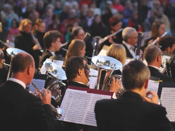 Ein Symphonieorchester spielt konzentriert live, während ein großes Publikum aufmerksam zuhört.
