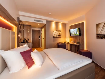 Stadtzimmer im Best Western Plus Hotel Stadtquartier Haan Modernes Hotelzimmer mit Doppelbett, warmem Licht, Flachbildschirm, Holzmöbeln und Schreibtisch.