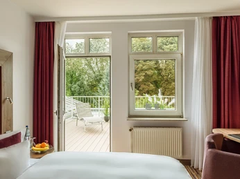 Parkzimmer im Best Western Plus Hotel Stadtquartier Haan Helles Hotelzimmer mit Zugang zu einer Terrasse, mit Blick auf grüne Bäume und ausgestattet mit gemütlichen Möbeln.