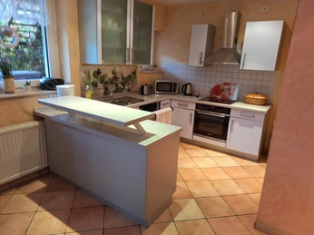 Küche in der Ferienwohnung Senjic in Heiligenhaus Moderne Küche mit hellem Fliesendesign, ausgestattet mit Backofen, Herd, Spüle und Dunstabzug.