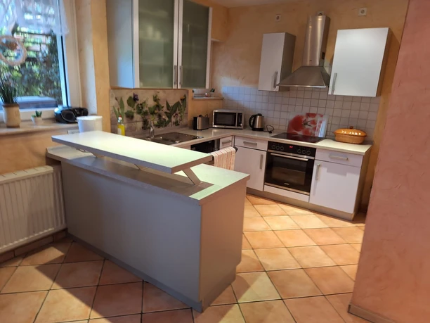 Küche in der Ferienwohnung Senjic in Heiligenhaus Moderne Küche mit hellem Fliesendesign, ausgestattet mit Backofen, Herd, Spüle und Dunstabzug.