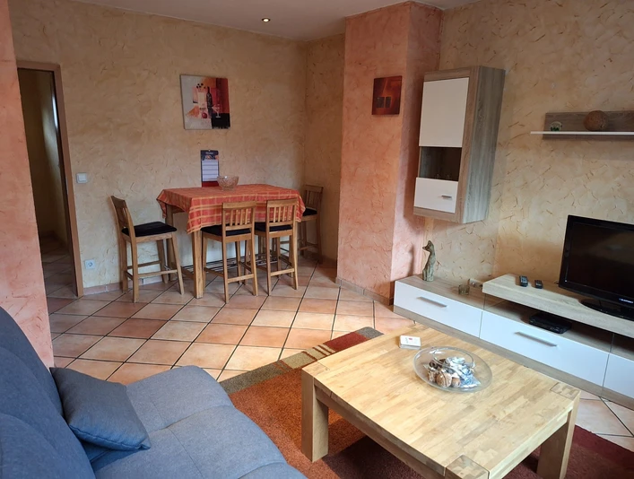 Wohnzimmer in der Ferienwohnung Senjic in Heiligenhaus Wohnzimmer einer Ferienwohnung mit Sofas, Esstisch, Stühlen und modernen Möbeln auf hellen Fliesen.