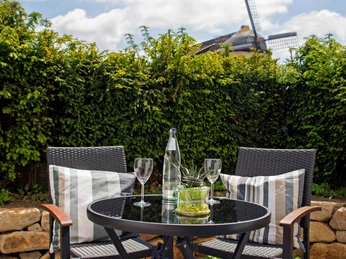 Boardinghouse am Teuto Lengerich -Terrasse.jpg Terrasse mit rundem Tisch und zwei Stühlen, flankiert von Hecken und einer Windmühle im Hintergrund.