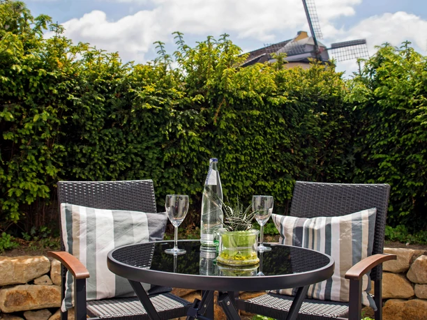 Boardinghouse am Teuto Lengerich -Terrasse.jpg Terrasse mit rundem Tisch und zwei Stühlen, flankiert von Hecken und einer Windmühle im Hintergrund.