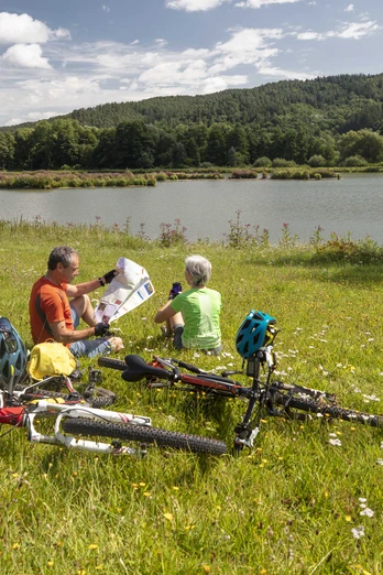 Rast am Regen Zwei Fahrradfahrer machen eine Rast am Ufer des Regens auf einer grünen Wiese