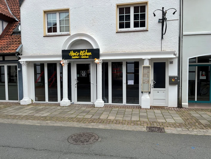 Das Restaurant Hani’s Kitchen präsentiert eine weiße Fassade mit großen Fenstern und einem gelben Logo.