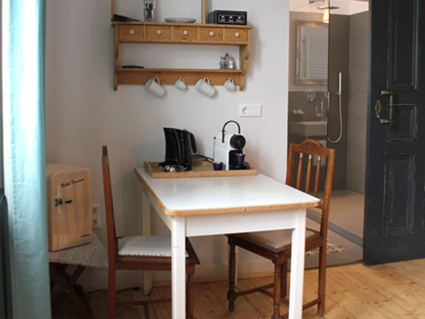 Küchentisch in der Fabrikantenvilla in Erkrath Ein kleiner Küchentisch mit zwei Stühlen steht vor einem Regal mit Tassen und Retro-Radio.