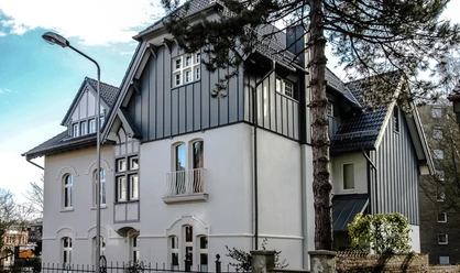 Fabrikantenvilla in Erkrath Eine prächtige Villa mit historischer Fassade und modernen Akzenten, umgeben von Bäumen und Zäunen.
