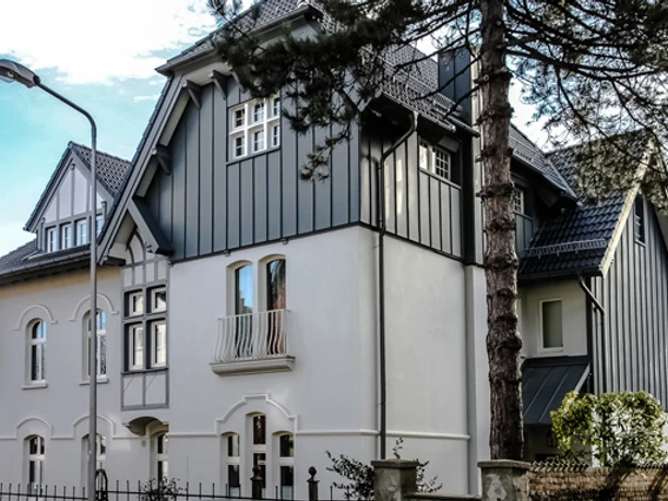 Fabrikantenvilla in Erkrath Eine prächtige Villa mit historischer Fassade und modernen Akzenten, umgeben von Bäumen und Zäunen.