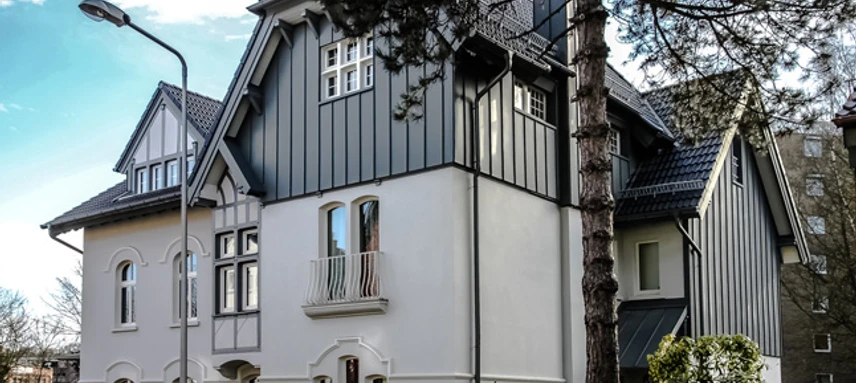 Fabrikantenvilla in Erkrath Eine prächtige Villa mit historischer Fassade und modernen Akzenten, umgeben von Bäumen und Zäunen.