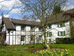 Gästewohnung Kleiner Bollenhof in Mettmann Das Bild zeigt eine Fachwerk-Gästewohnung mit weißen Wänden und grünen Fensterläden, umgeben von Natur.