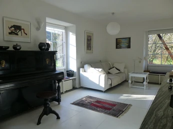 Wohnbereich in der Gästewohnung Kleiner Bollenhof in Mettmann Ein heller Wohnbereich mit Sofa, Teppich, Klavier und Kunst an den Wänden lädt zur Entspannung ein.