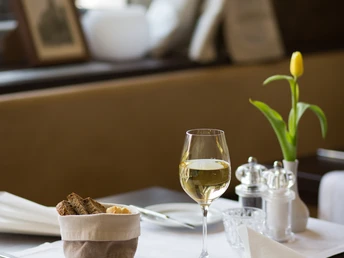 Restaurant im Hotel und Restaurant Haus Fabry in Hilden Ein gedeckter Tisch mit Weißwein, Brot, Butter und einer gelben Tulpe unter sanftem Tageslicht.