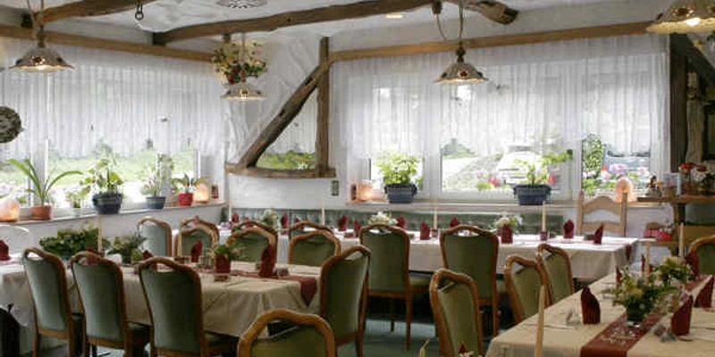 Gastraum im Hotel und Restaurant Haaner Hof in Haan Gemütlicher Gastraum mit rustikalem Holzgebälk, gedeckten Tischen und großen Fenstern mit Blumenschmuck.
