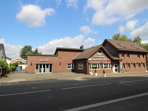 Hotel und Restaurant Haaner Hof Das Bild zeigt ein Backsteingebäude mit Restaurant Haaner Hof, umgeben von Bäumen und blauen Himmel.