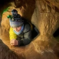 Kleine Höhlenforscher in der Sächsischen Schweiz Kind mit Mütze und Stirnlampe kriecht durch einen engen, sandfarbenen Höhlentunnel. Die Atmosphäre wirkt abenteuerlich und konzentriert.